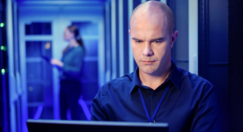 Male IT engineer using laptop in server room.